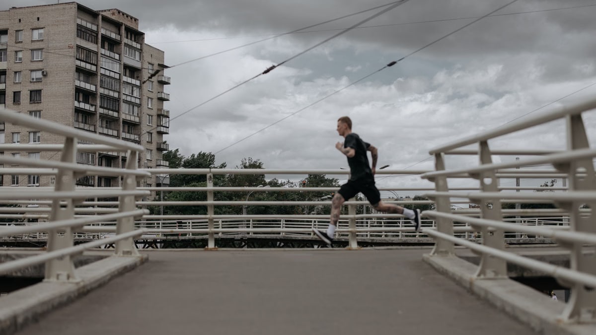 A man runs on a city bridge under cloudy skies, showcasing an active lifestyle.